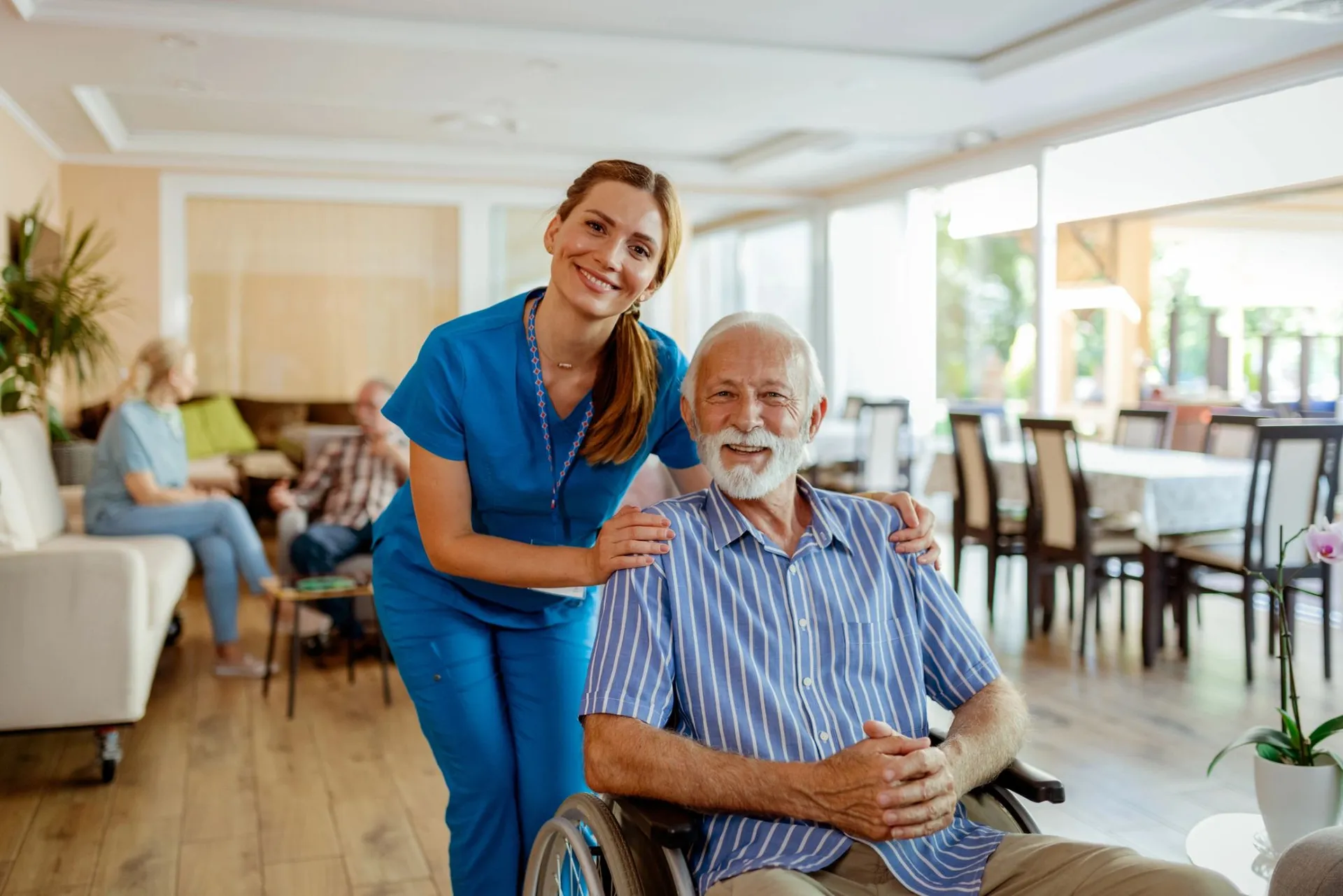 Caregiver smiling beside an older man in a bright home